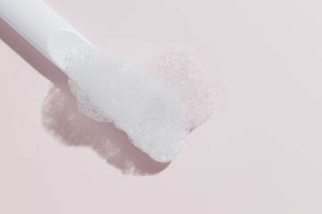 Foamy cleanser on white spatula, pastel pink background.