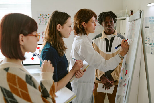 Diverse team engaged in scientific discussion around whiteboard, presenting ideas and sharing thoughts in laboratory environment