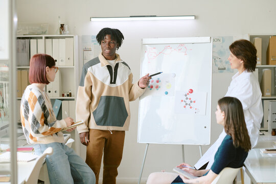 Group of professionals discussing project plan during lesson with charts on whiteboard, sharing ideas and notes. Setting seems collaborative with focus on teamwork