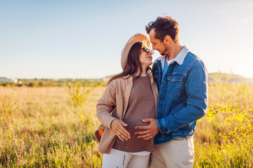 Pregnant family couple walking outdoors. Future parents in love hugging enjoying sunset