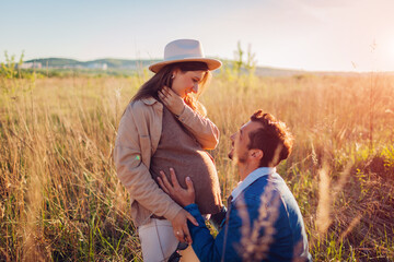 Young pregnant family couple walking outdoors. Future father touching his wife's belly.