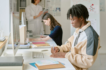 Obraz premium Student focusing on studies at modern classroom while others working in the background. Technology and devices enhancing the learning experience