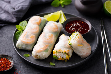 Vietnamese food. Spring rolls with shrimps and vegetables on a black plate. Grey background. Close up.