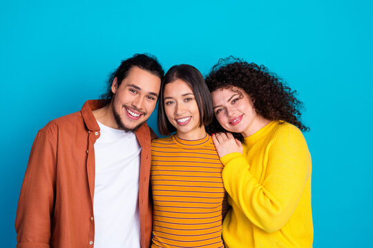 Group of three young diverse friends embracing on blue background, showcasing happiness, togetherness, friendship and casual lifestyle