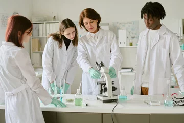 Fotobehang Team of researchers observing and discussing experiment under microscope in laboratory setting. Researchers wearing lab coats and gloves, engaging in scientific analysis © AnnaStills