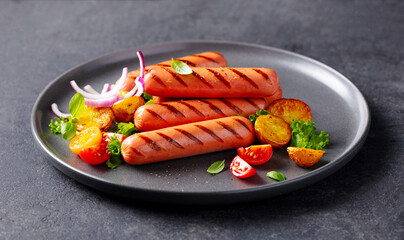 Sausages with potatoes and onion on a black plate. Grey background. Close up.
