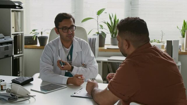 Young confident doctor in medical uniform making presentation of insulin pen to male patient and explaining him how to make injections during consultation in clinical office
