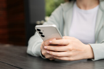 Close-up of hands holding and using a modern smartphone outdoors, showcasing technology and...