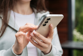 Close-up of hands holding and using a modern smartphone outdoors, showcasing technology and connectivity in daily life.