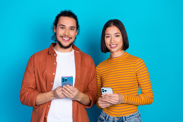 Smiling young friends holding smartphones against a vibrant blue background, showcasing casual...