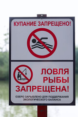 Warning Sign In Russian Language "Kupanie Zaprescheno" (No Swimming) And "Lovlya Ryby Zapreschena" (No Fishing) By A Lake.