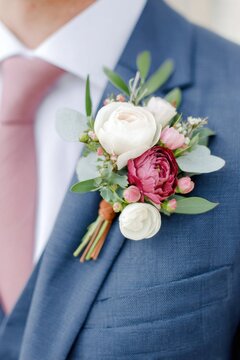 Elegant floral boutonniere featuring white, pink, and deep red blooms, adorned with greenery, attached to a tailored blue suit, enhancing formal attire for special occasions