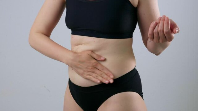 Slimming cosmetics. A close-up of the belly of a young woman who smears her skin with cream or lotion. The woman is massaging the skin on her stomach. Anti-cellulite massage.