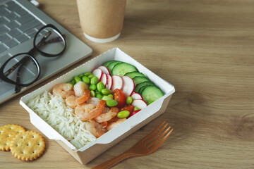 Lunch break. Rice with shrimps and vegetables in paper take away box on desk