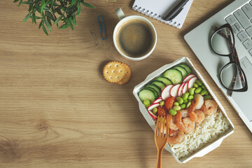 Lunch time in office. Rice with shrimps and vegetables in paper take away box on desk