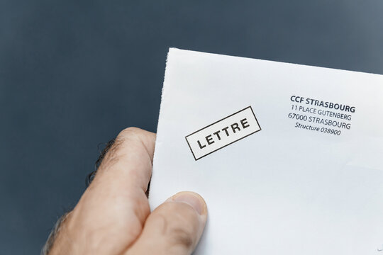 Paris, France - Oct 28, 2024: A hand holds a white envelope with the word LETTRE stamped on it and an address for CCF Strasbourg at 11 Place Gutenberg, 67000 Strasbourg