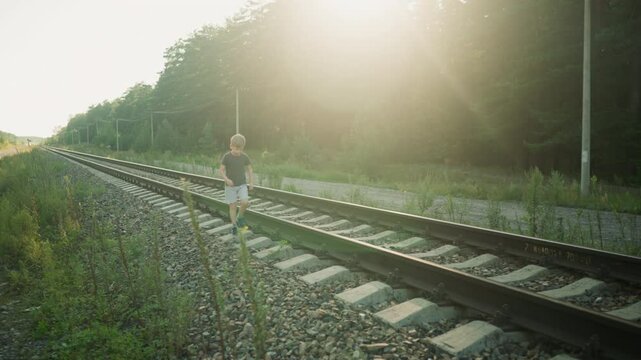kid in casual outfit playfully jumping on rail sleeper along quiet railway surrounded by nature, with golden sunlight casting warm glow on forest background