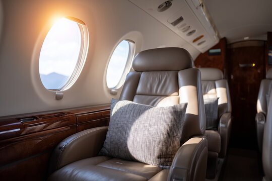 Luxury private jet interior with leather seats, wood paneling, and ambient lighting, natural sunlight streaming through oval windows, clean and modern aesthetic.