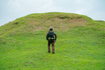 A male adventurer is enjoying the beauty of a small hill covered in green grass. The Asian male traveler is relaxing on the clean and beautiful green hills.