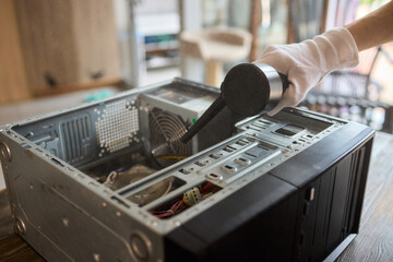 A man cleans a computer case with a vacuum in a bright room, stressing workspace tidiness