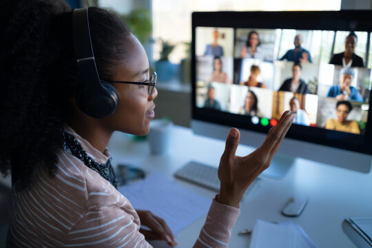 Young adult Black woman hosting a virtual roundtable discussion, wearing headphones and actively engaging with other professionals onscreen