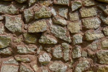 Wall fence of stones of different sizes roughly stacked on top of each other and fastened with cement. Construction industrial background.