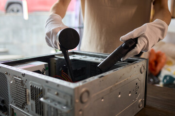 A man cleans a computer case with a vacuum in a bright room, stressing workspace tidiness