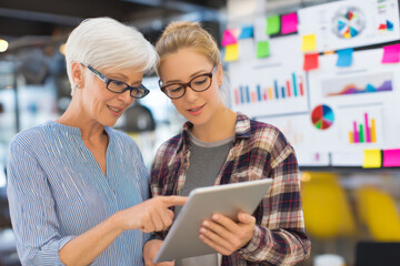 Mature Caucasian woman mentoring a junior analyst on data visualization techniques, pointing to colorful charts on a tablet