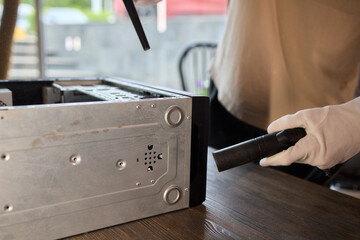 A man cleans a computer case with a vacuum in a bright room, stressing workspace tidiness