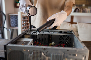 A man cleans a computer case with a vacuum in a bright room, stressing workspace tidiness