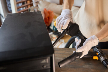 A man cleans a computer case with a vacuum in a bright room, stressing workspace tidiness