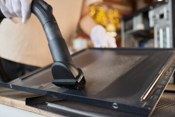 A man cleans a computer case with a vacuum in a bright room, stressing workspace tidiness