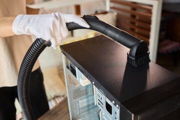A man cleans a computer case with a vacuum in a bright room, stressing workspace tidiness