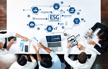 A diverse business team engages in a strategic discussion about ESG principles, analyzing data and...