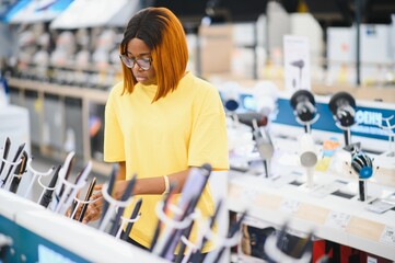 Girl standing at the counter in the store of electronic equipment choosing a new Curling iron to buy