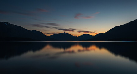 Tranquil Waters: A mesmerizing dusk scene unfolds as a serene lake mirrors the silhouettes of majestic mountains, creating a stunning display of nature's beauty.
