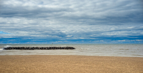 A section of a beach on Lake Erie at Presque Isle State Park, Pennsylvania, with a breakwater and a tiny sailing ship visible on the horizon