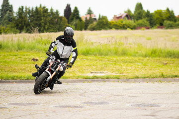 Obraz premium Man in a black biker suit and helmet performs extreme stunts on a motorcycle in mid-air. Dynamic pose, powerful bike, dramatic angle, and blurred outdoor background.