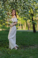 Beautiful Girl with long hair in a white dress poses near white blossoming apple trees