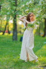 Beautiful Girl with long hair in a white dress poses near white blossoming apple trees