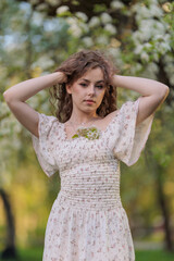 Naklejka premium Beautiful Girl with long hair in a white dress poses near white blossoming apple trees