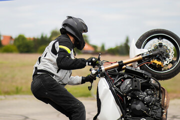 Man in a black biker suit and helmet performs extreme stunts on a motorcycle in mid-air. Dynamic...