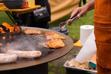 Grilling meat and sausages outdoors with african male chef using tongs
