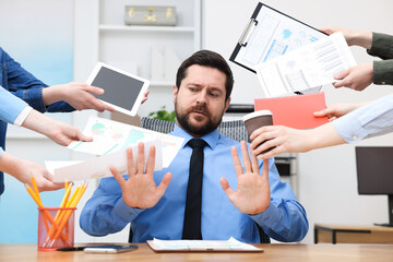 Man overwhelmed by different requests from colleagues at desk in office