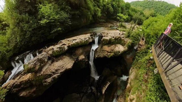 Woman standing on metal walkway, contemplating stunning waterfalls and lush greenery of Abasha River flowing through Martvili Canyon in Georgia