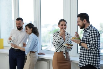 Obraz premium Colleagues with food and drinks near window in office during lunch break