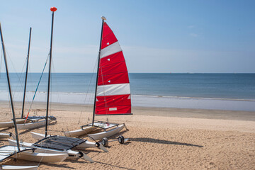 A catamaran on a sandy beach in Brittany, with its red and white sail
