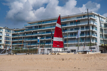 A catamaran on a sandy beach in Brittany in the town of La Baule, with its red and white sail in front of apartment blocks