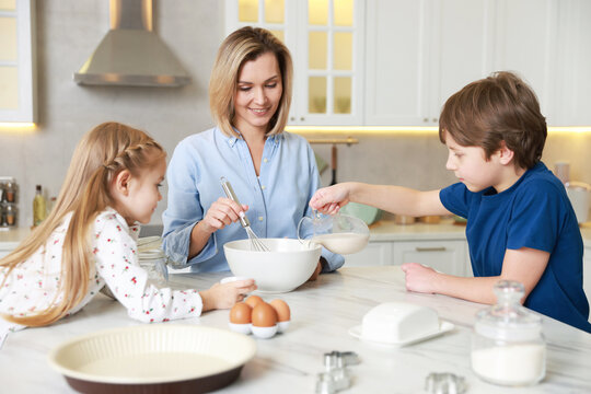 Mother and her kids making dough at white marble table in kitchen