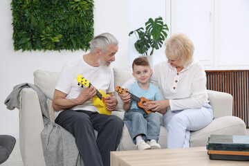 Grandparents teaching their grandson to play guitar on sofa at home